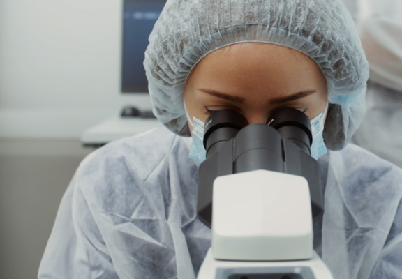 A woman in a laboratory looks into a microscope.