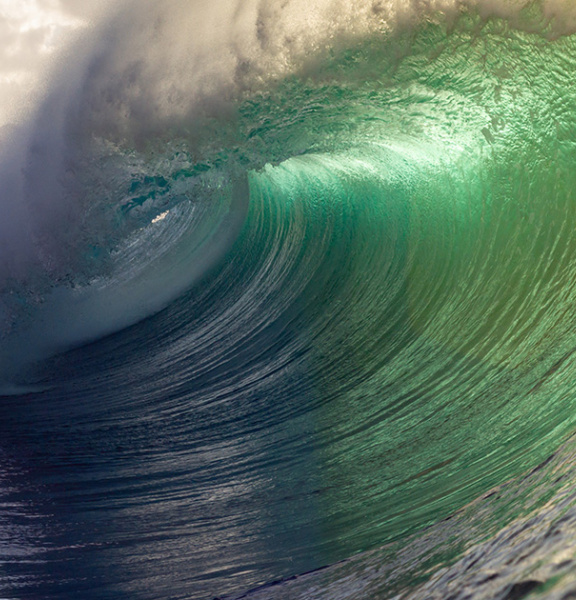 Picture of a wave, bright green with mountains in the background.